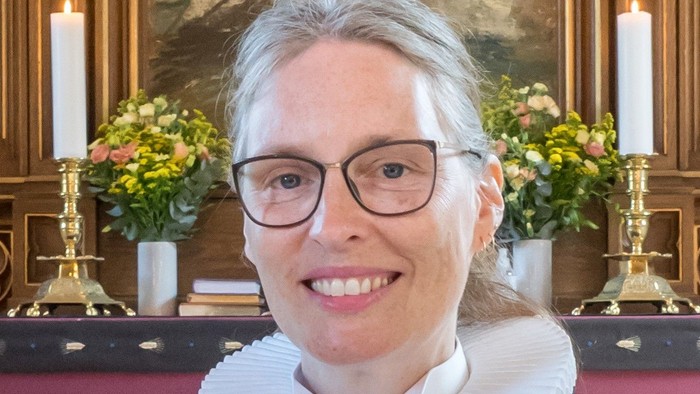 Kvinde i sort kapelrob med hvid krage og briller.