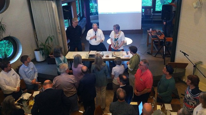 Ein Mann präsentiert vor einem Publikum, das um Tische sitzt.