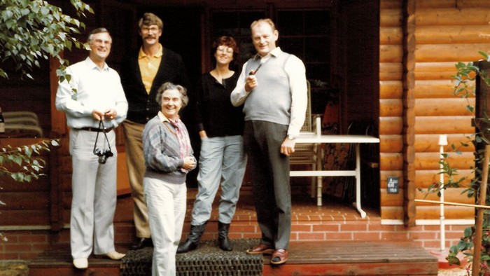Eine Gruppe von fünf Personen steht vor einer Holzhütte und posiert für ein Foto.