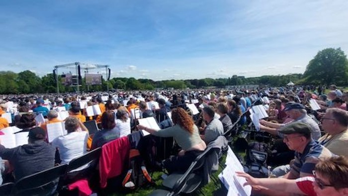 Große Menschenmenge sitzt auf Stühlen im Freien bei gutem Wetter