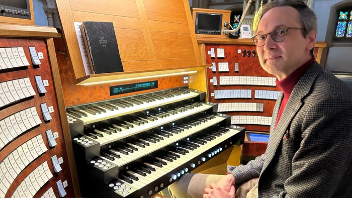 Mann sitzt an einer Kirchenorgel und schaut in die Kamera