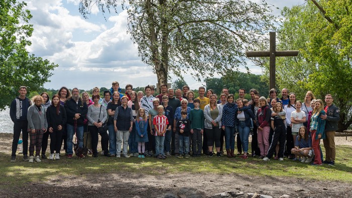 Eine große Gruppe von Menschen posiert vor einem Kreuz im Freien