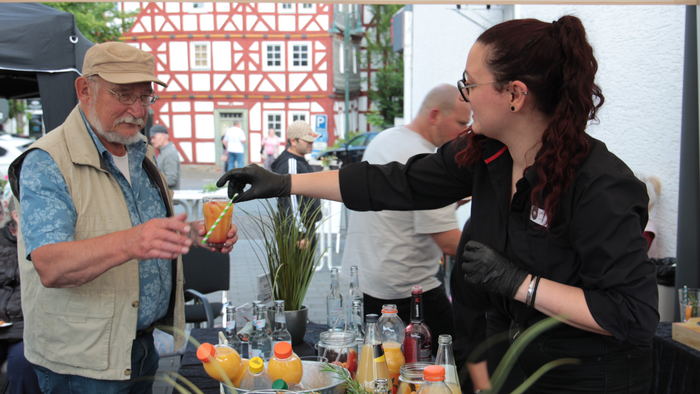 Ein Mann und eine Frau stehen an einem Stand mit Getränken, die Frau hält ein Glas.
