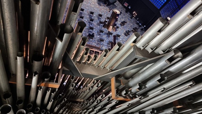 Ein großer Raum mit zahlreichen Metallrohren und einer bunten Deckeninstallation.