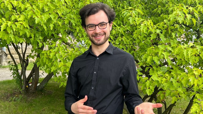 Mann in schwarzem Hemd vor grünem Baum