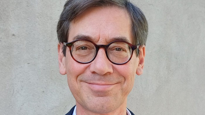 Mann mit Brille und Anzug vor grauer Wand