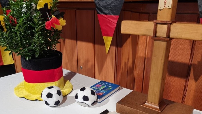 Auf dem Tisch stehen ein Kreuz, eine Bibel, eine deutsche Flagge und ein Fußball.
