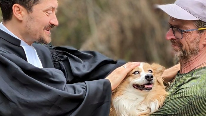 Zwei Männer halten einen freudigen Hund zwischen sich.