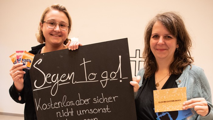 Zwei Frauen halten ein Schild mit Segenssprüchen und Snacks