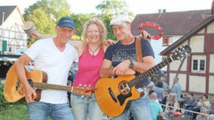 Drei Personen posieren mit Gitarren vor einem Gebäude.