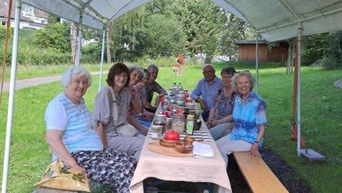 Eine Gruppe von Menschen sitzt unter einem Zelt an einem Picknicktisch im Freien.