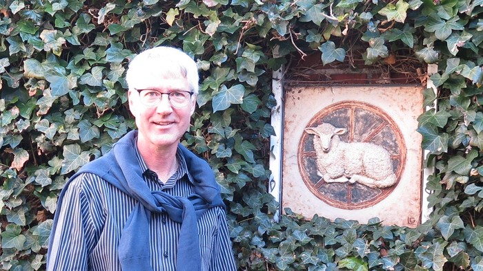En mand står foran en mur dækket af ege og en plaket med et skjold og et dyr.