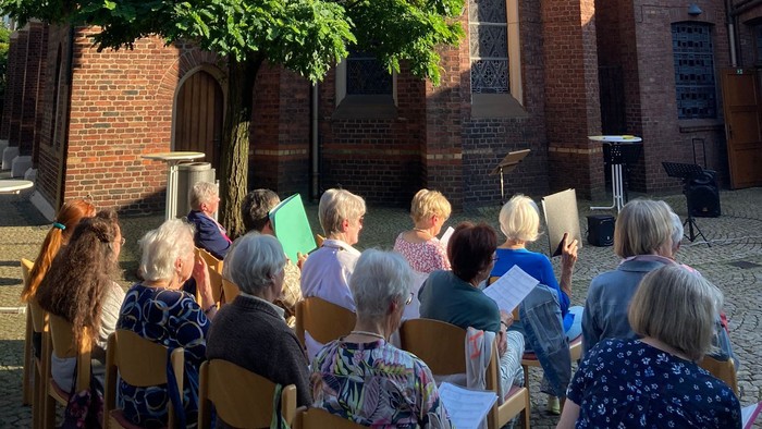 Gruppe von Menschen sitzt vor alter Kirche auf Stühlen