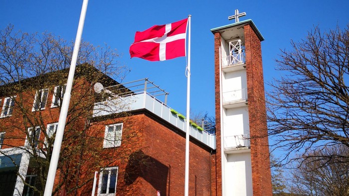 Toppen af klokketårn med kors og to danske flag.