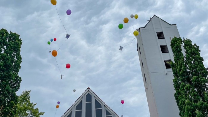 Farbenfrohe Ballons steigen vor weißer Kirche auf
