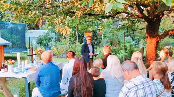 Andacht unter Bäumen mit Altar und Besuchern. Garten im Hintergrund