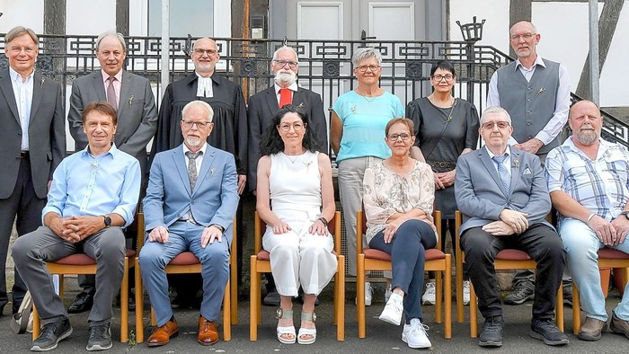 Gruppe von Menschen, die für ein Foto posieren, einige stehen, andere sitzen auf Stühlen.