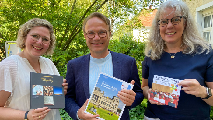 Drei Personen halten Bücher in die Kamera und lächeln