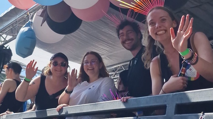 Eine Gruppe von Menschen feiert auf einem Festwagen mit Luftballons und einem Banner.