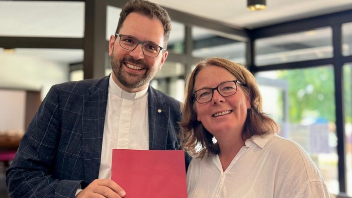 Ein Mann und eine Frau halten ein rotes Dokument und lächeln.