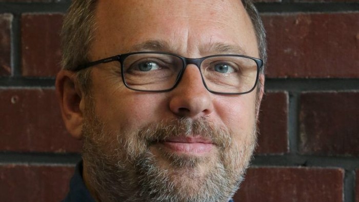 Mann mit Brille und Bart vor Ziegelmauer