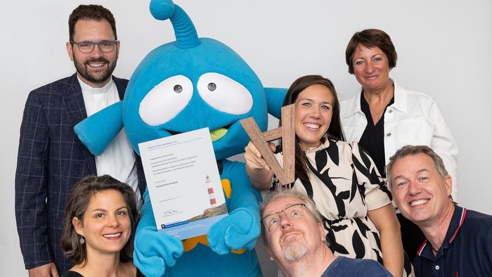 Ein Team posiert mit einer blauen Figur, die ein Tablet hält.