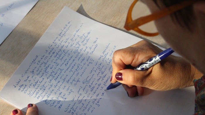 Person schreibt mit blauem Stift auf Papier