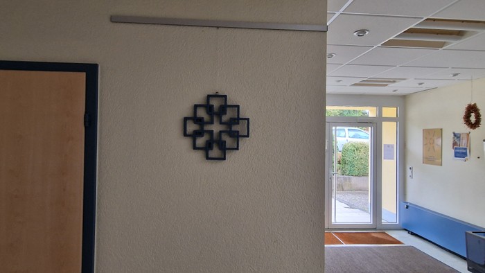 Ein Flur mit einem Kreuz an der Wand und einer Tür, die zu einem Raum mit Bildern führt