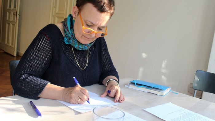 Frau sitzt am Tisch und schreibt mit einem Stift