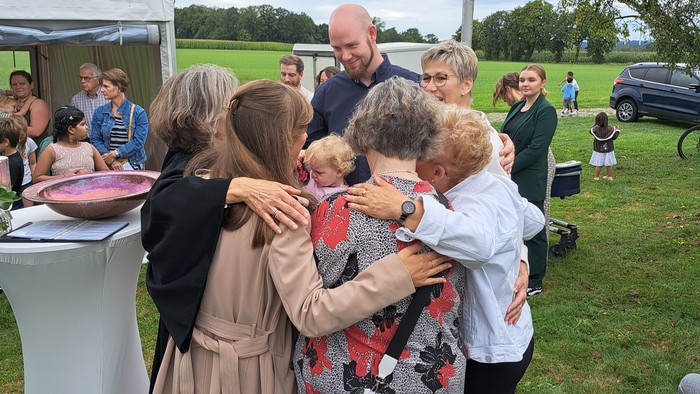 Eine Gruppe von Menschen umarmt sich auf einem grasbewachsenen Feld bei einer Veranstaltung.