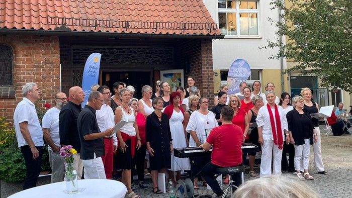 Eine Gruppe von Menschen versammelt sich vor einem Gebäude mit rotem Dach und feiert.