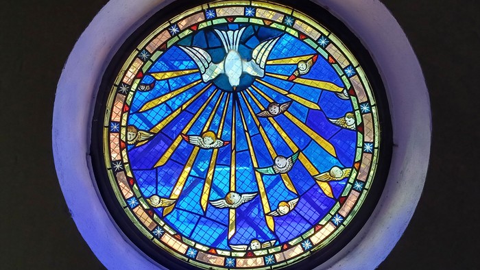 Ein buntes Kirchenfenster mit einem kreisförmigen Design und Strahlen, die von einem zentralen Punkt ausgehen