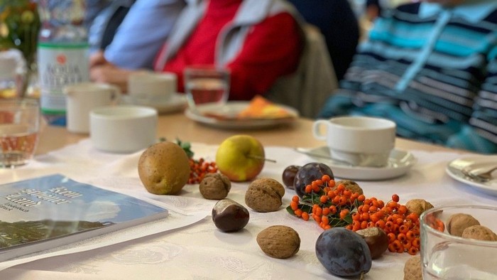 Ein Tisch mit verschiedenen Früchten, Teetassen und Menschen im Hintergrund