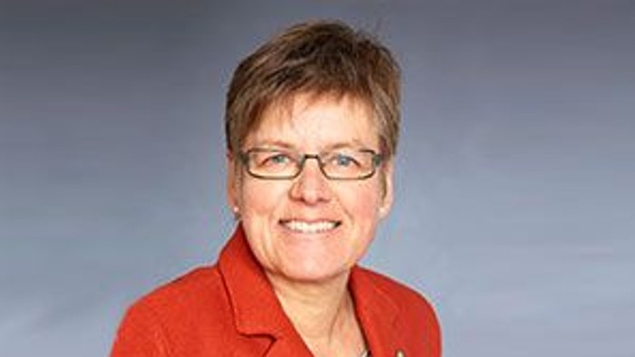 Eine Frau mit kurzem Haar und Brille trägt eine rote Jacke und lächelt.