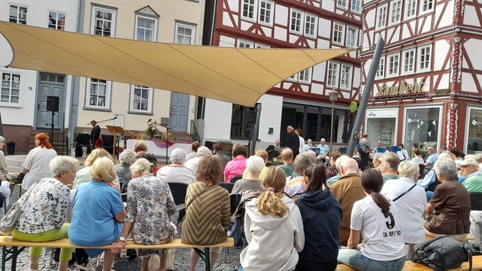 Große Freiluftveranstaltung mit Menschen, die an langen Tischen unter einem Baldachin sitzen.