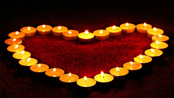 Herzförmige Anordnung von brennenden Kerzen auf rotem Stoff