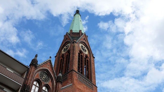 Ein roter Ziegelbau mit Uhrturm und grünem Dach unter blauem Himmel