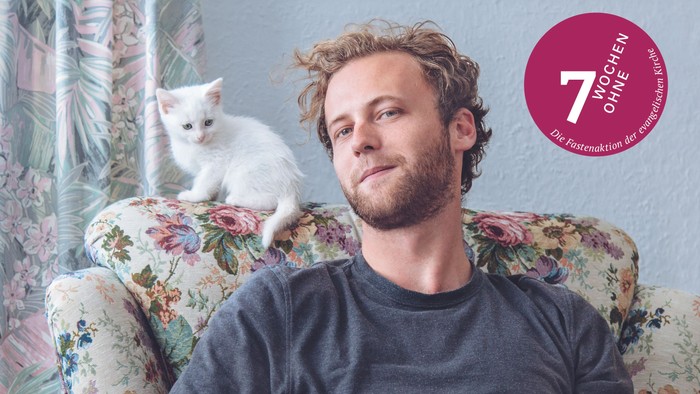 Das Aktionsmotiv 2026 der Fastenaktion 7 Wochen ohne: Ein Mann auf einem geblümten Sessel. Auf der Lehne sitzt eine weiße Katze.