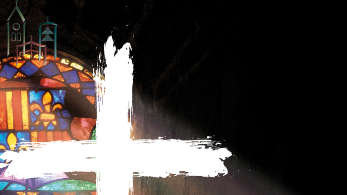 Ein weißes Kreuz vor buntem Glasfenster in einer Kirche