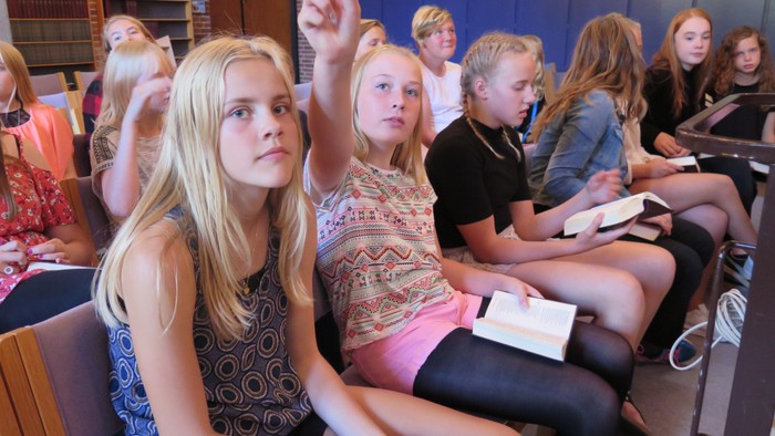 En gruppe skolepiger i klassesalen med en pige der hejer hånden.