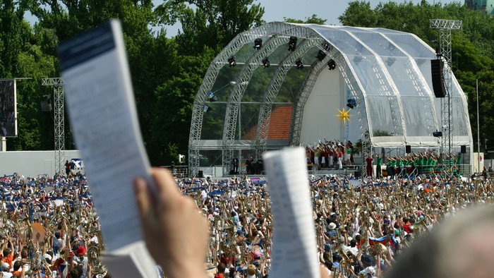 Große Menschenmenge bei Freiluftkonzert, viele halten Blätter hoch