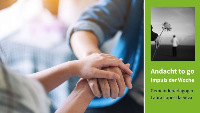 Zwei Personen halten sich an den Händen, eine Blume in der Natur