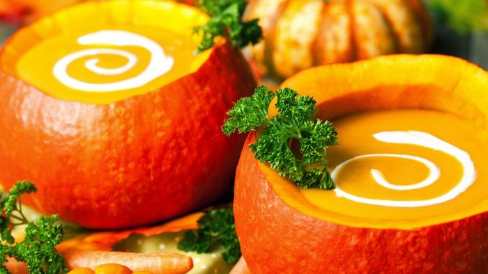 Zwei Kürbisschalen mit Suppe und Petersilie, umgeben von Gemüse