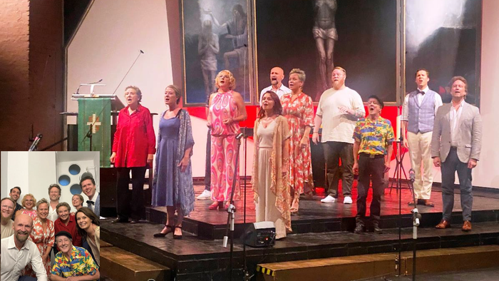 Eine vielfältige Gruppe tritt in farbenfroher Kleidung während eines Chor-Konzerts oder einer musikalischen Veranstaltung auf der Bühne auf.