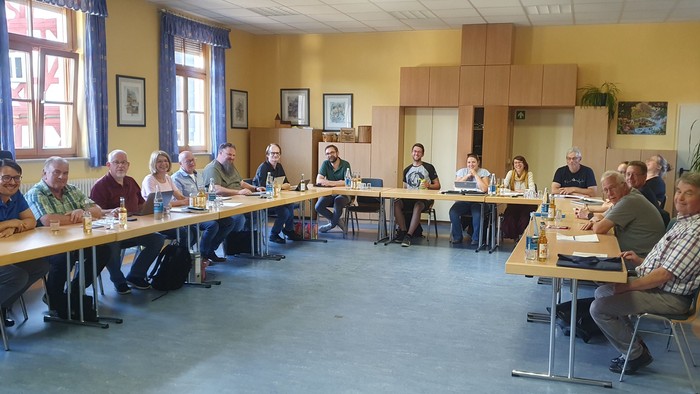 Eine Gruppe von Menschen sitzt in einem Raum an Tischen und arbeitet.