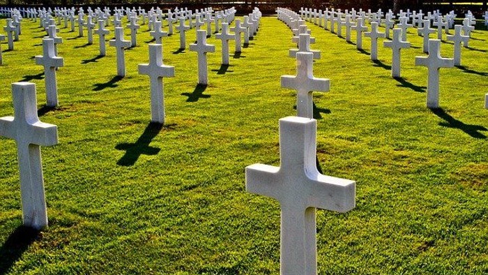 Sorgfältig angeordnete weiße Kreuze auf einem gepflegten Soldatenfriedhof im saftigen grünen Gras.