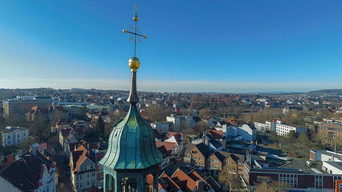 Die Stadtlandschaft mit einem grünen Kirchturm und goldener Wetterfahne unter klarem Himmel.