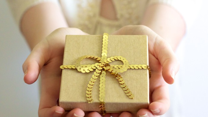 En person holder en lille pakke med guldfarvet snurrebånd.