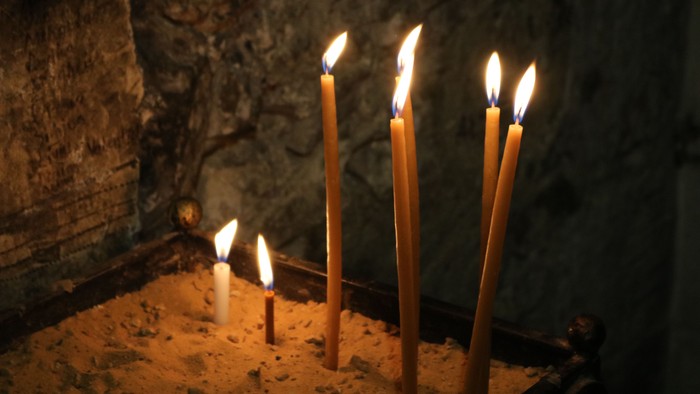 Drei brennende Kerzen vor Steinwand