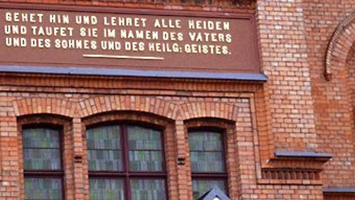 Das Bild zeigt ein Zitat auf einem Ziegelgebäude mit einer Statue daneben.